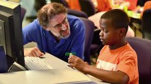 Mitch Resnick and a young boy talk while sitting at a computer.