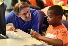 Mitch Resnick and a young boy talk while sitting at a computer.