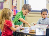 three children working at a desk with hands-on materials