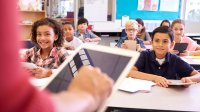 Students use tablets for formative assessment while a teacher in the foreground leads them.