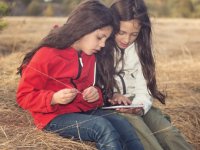 Two young girls sitting outside looking at a tablet device