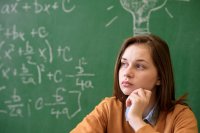 A teenage girl sitting in front of a blackboard with math formulas written on it, looking thoughtful