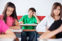 Student sitting at a desk in the back of a classroom, taking a moment to collect himself