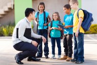 Teacher kneeling next to four elementary school students, smiling