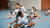 Middle school student stretches with teacher in gym class