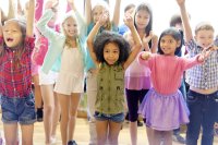 A group of elementary school students standing with their arms in the air.