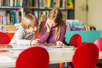 Two kids of different grade levels reading together in a library