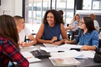 A teacher talking to her high school students at a table in a classroom