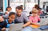 A teacher helping students on their laptops