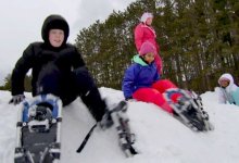 Four students wearing snow shoes sitting on a mound of snow