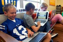 Three kids sitting in class on a big futon each with a laptop