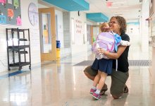 Teacher kneels down to embrace a hug from a young student