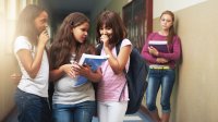 Three girls exclude another girl in a school hallway.