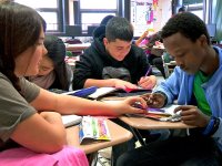 Four students, desks in a circle, working as a group; one helping another with a math problem