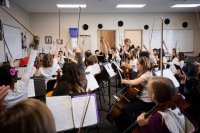 A middle school music class of bowed instrument players, all raising their bows in the air before playing