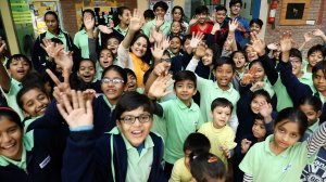 A large group of students and their teacher are smiling and waving.