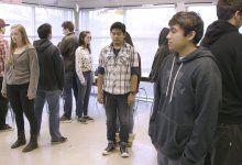 A class filled of high school students are standing back-to-back with their eyes closed, focusing on their breath.