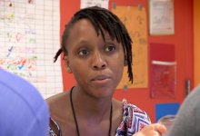 A close up of a female teacher from the shoulders up. She's sitting at a table with two other teachers, talking. 