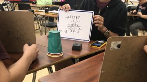 Students reviewing each other's math problems written on small whiteboards