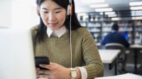 A female student listens to music and checks her phone while doing schoolwork.