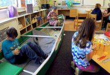 Kids working independently sitting in a canoe, and in groups at a small round table and a square table at floor height