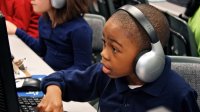 Young boy with some very large headphones working at a computer station