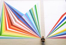 Girl standing in front of an outdoor mural of rainbow rays.