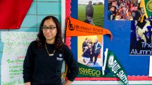 WHEELS student standing by bulletin board with college flags.