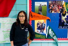 WHEELS student standing by bulletin board with college flags.